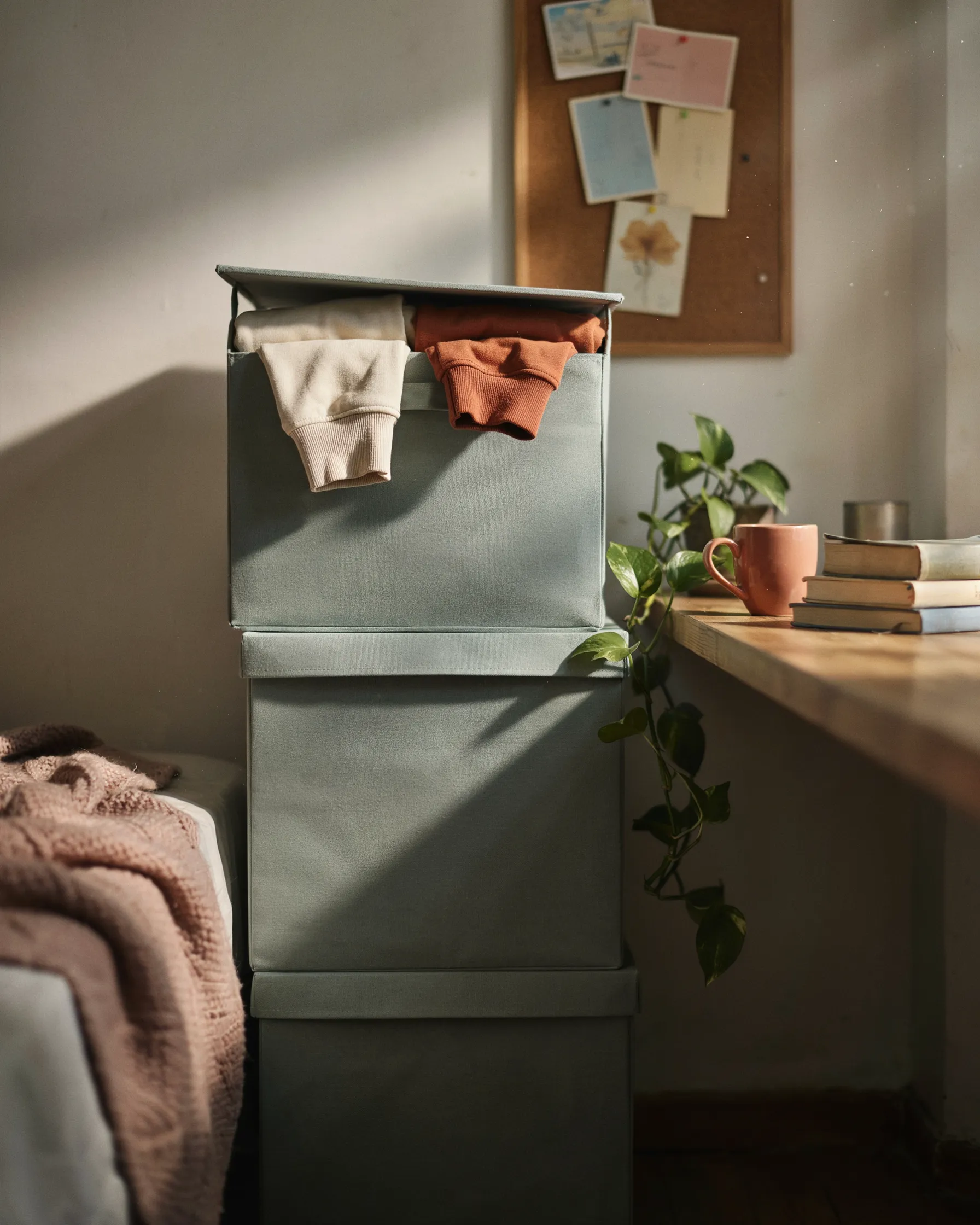 Stacked fabric storage cubes in a dorm room corner beside a desk, with folded sweaters tucked in the top cube